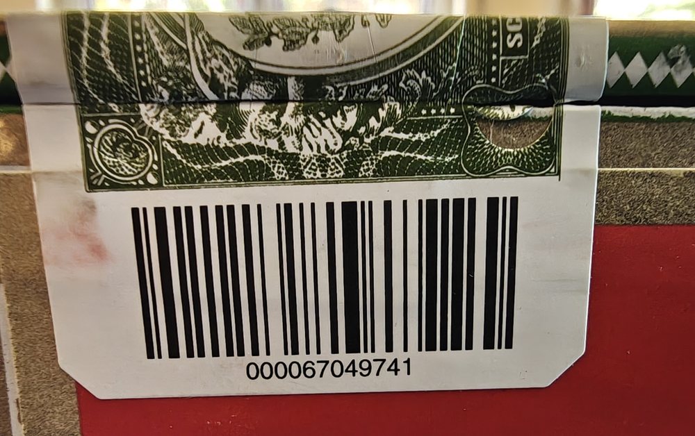 Das grüne Siegelpapier über der Kistenkante, darunter der Barcode mit der Kistennummer in Klarschrift.