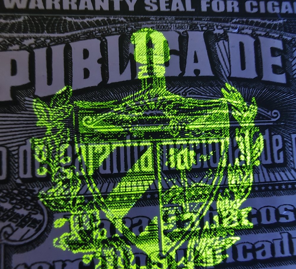 Dasselbe Siegel unter UV-Licht: das kubanische Wappen leuchtet hellgrün auf, im Tageslicht ist davon nichts zu sehen.
